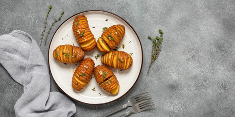 Homemade baked Hasselback Potato with fresh herbs in a plate. Gray grunge background. Top view,...