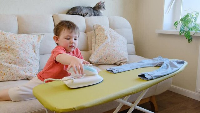 Child left without supervision may get burned or hurt as the baby plays dangerously with a hot iron in the living room of the home. Kid aged about two years (one year ten months)