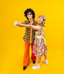 Asian hippie couple dress in 80s vintage fashion with colorful retro clothing while dancing together isolated on yellow background for fancy outfit party and pop culture concept