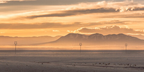 Transmission power lines at sunset on the high plains of New Mexico with Sandia Mountains in the...