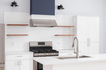 A kitchen detail with white cabinets, floating wood shelves on a white subway tile backsplash, and...