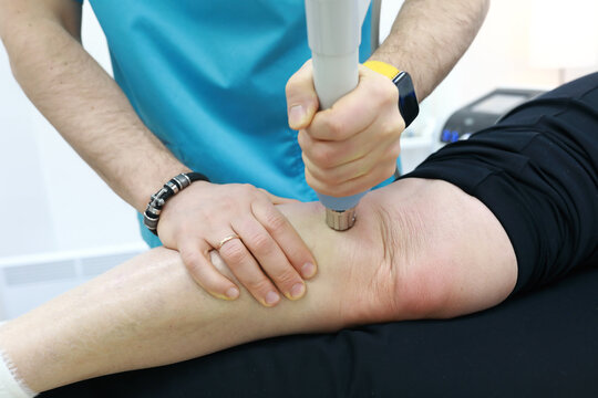 Osteopath treating knee to woman with shock wave therapy