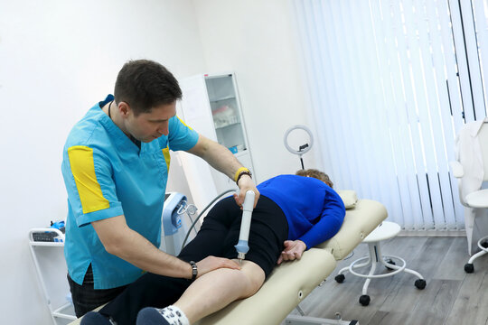 Osteopath treating senior woman's leg with shockwave therapy