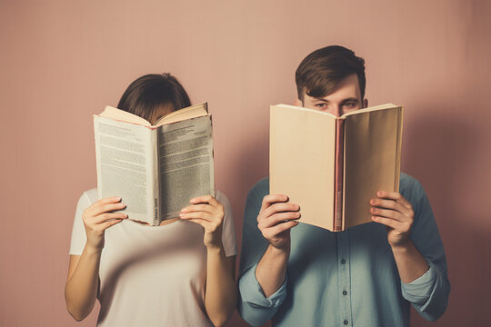 Young couple reading with books obscuring faces