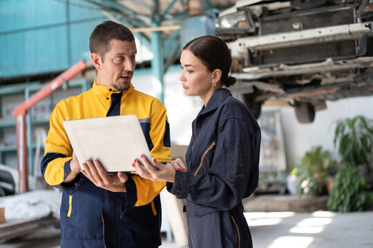 Caucasian man and woman mechanic talking with team and use notebook computer with car lift background at car service	