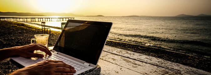 Working on laptop on beach on wooden table at sunset. High resolution photo image can be used as...