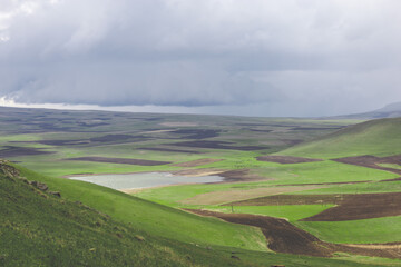 Top view shot of highland lake and the field covered with vibrant lush green grass on a picturesque, cloudy spring day. Agrarian land in springtime.