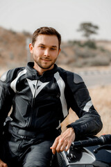 Guy biker in leather jacket looking at the camera sitting on motorcycle. Selective focus