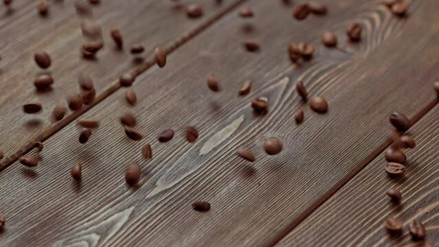 brown roasted coffee beans sprinkling on wooden board surface - full frame close-up slowed down four times