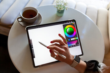 A girl in a cafe draws with a stylus on a graphics tablet.