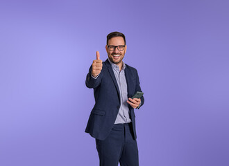 Cheerful male entrepreneur gesturing thumbs up after reading good news over smart phone. Happy...