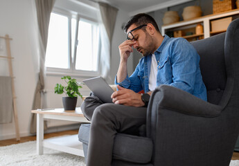 Fototapeta premium Anxious male computer programmer with headache working on laptop. Frustrated young freelancer solving technical and software virus problems over wireless computer in home office