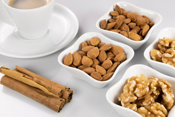 Café con canela en rama y frutos secos en fondo blanco