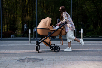 Portrait of a beautiful girl. Close-up photo of a beautiful girl in a plaid shirt and a white cap. The girl stands near the brown baby carriage. Mother walking with a small child