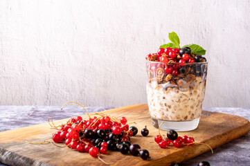 Currants and granola with yogurt in a glass. Currants are scattered on the board.
