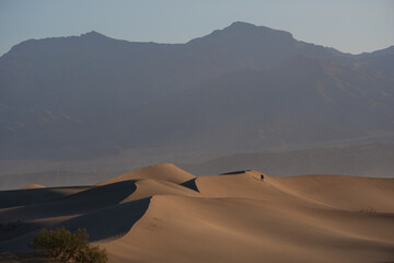 Fototapeta na wymiar Death Valley, USA. Man climbing a sand dune, with mountains in the background
