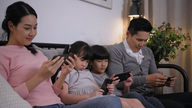 Family concept of 4k Resolution. Asian parents and children playing with mobile phones in the living room.