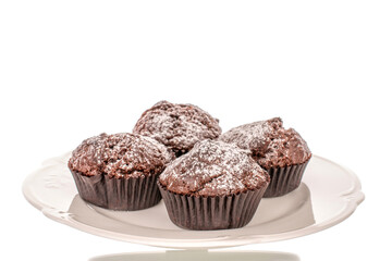 Four homemade chocolate muffins on a white ceramic plate, macro, isolated on a white background.