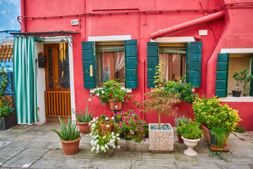 Fototapeta na wymiar Door and window with flower on the red facade of the house. Colorful architecture in Burano island, Venice.