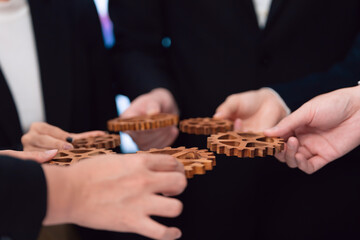 Closeup hand holding wooden gear by businesspeople wearing suit for harmony synergy in office...