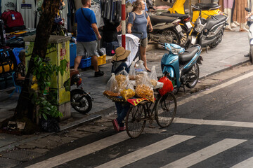 People, vendors, bicycles and cyclo drivers taking tourist on a busy, bustling street in the old...