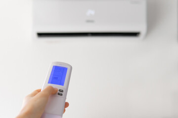 hand with air conditioner remote control. turning on the air conditioner close-up with a blurred background. climate control.