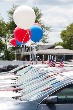 Balloons and American flags on cars at automobile dealership.