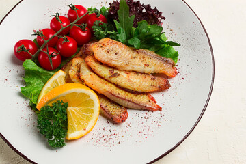 Fried Tilapia fish fillet, in spices, with cherry and salad, on a white plate, homemade, no people,