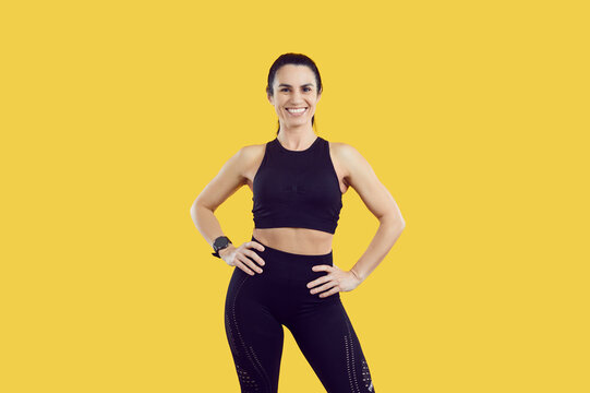 Beautiful self-satisfied Caucasian woman smiling looking at camera posing for banner advertising fitness club or sporting event, wearing tight workout clothes stands on yellow background