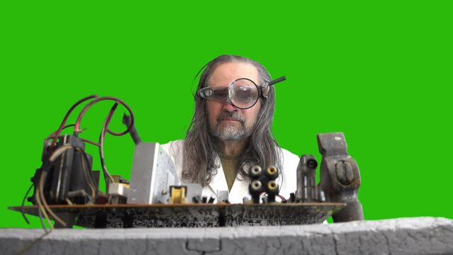 Crazy computer repairman repairing motherboard with hammer and soldering iron, soldering with smoke and showing like. Elderly man with magnifying glass and flashlight on his forehead with long hair