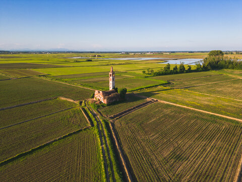 Aerial view of abandoned church in the middle of the wheat fields with rise fields in background. Novara, Piedmont