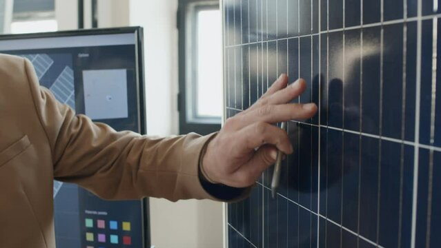 Close-up shot of hand of unrecognizable male engineer with pencil explaining configuration and design of innovative new solar panel, in front of multimedia screen with presentation, in office