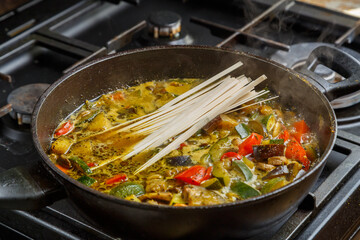 A frying pan with stewed vegetables in sauce and spices contains udon.