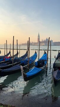Vertical video of a beautiful sunrise in Venice, Italy where you can see the sea, the gondolas and old buildings.