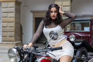 Naklejka na ściany i meble Sexy young woman with long black hair is sitting on vintage motorcycle. Horizontally. 
