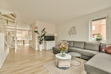 a living room with wood flooring and white walls, including a large gray couch in the center of the room