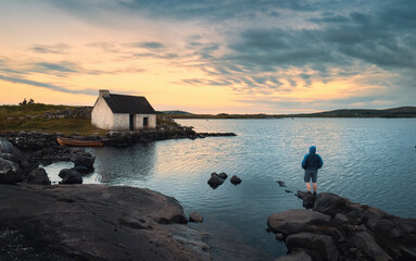 Beautiful sunset nature scenery with man on the rock watching sunrise at Fisherman's hut, screebe,...