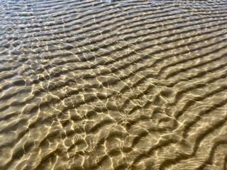 Fototapeta na wymiar Transparent sea water and sandy bottom, ripples on the sea water, natural sea water background