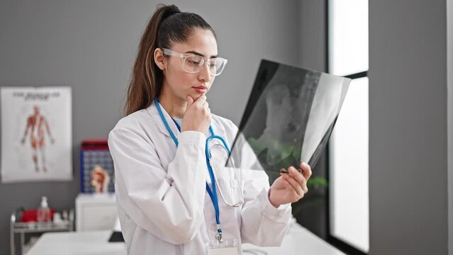 Young beautiful hispanic woman doctor looking xray standing at clinic