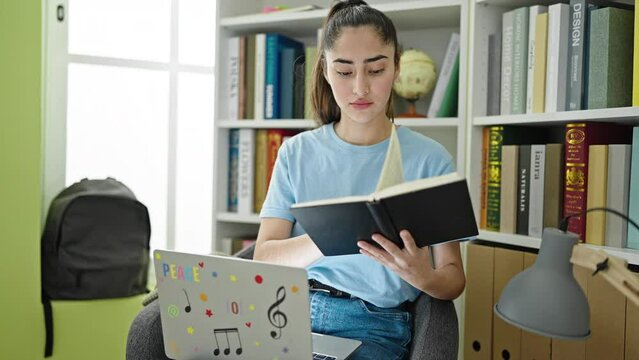 Young beautiful hispanic woman student reading book using laptop at library university