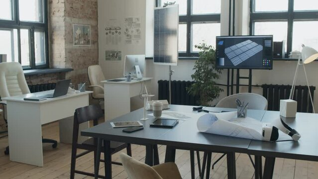 Full pan shot of creative renewable energy engineering company office, in loft style, with white furniture, computers, screen with solar panels presentation, posters, plans and wind turbine model