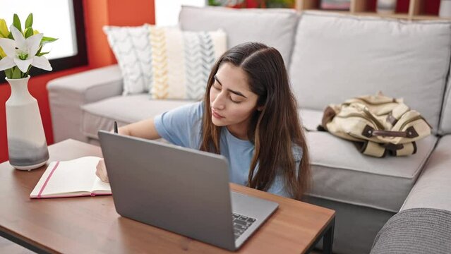 Young beautiful hispanic woman using laptop taking notes at home