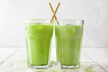 Iced green matcha latte in glasses with a straw on white background. Cold summer drink