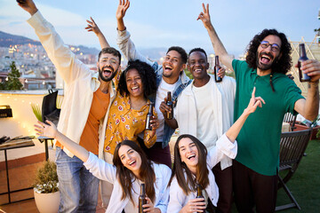 Group of diverse excited friends celebrating with beers at barbecue party in attic. Portrait of...