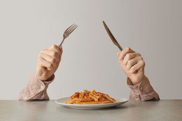 Male hands with a knife and fork next to a plate of pasta with tomatoes and cheese