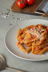 Pasta on a fork with tomatoes and cheese in a plate on a gray background