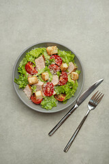 Vegetable salad with chicken and cheese on a gray table. Caesar salad in a gray plate.