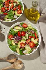 Fresh green salad with tomatoes, cucumbers, radish, sweet pepper and avocado in a white plate on a gray background.
