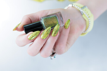 Female hand with long nails and a bottle of bright yellow green nail polish