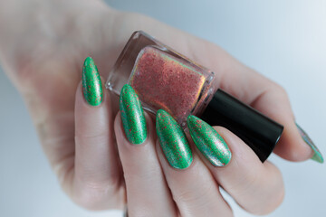 Female hand with long nails and bright green manicure with bottles of nail polish